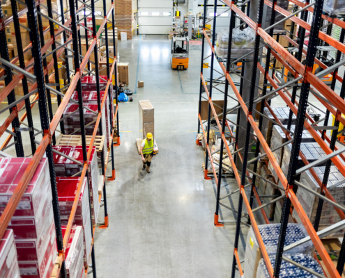 Warehouse worker pulling a pallet truck between shelves, above view